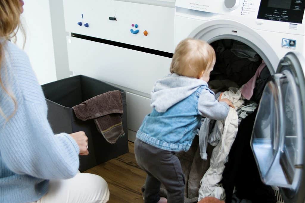 importance of routine for autism. A little boy helps his mom load clothes into the dishwasher.
