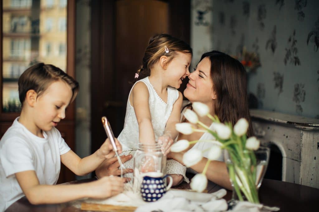 importance of routine for autism. A girl and a boy sit at the kitchen table with their mom. The boy is mixing in a bowl and the girl and mom put their noses together.