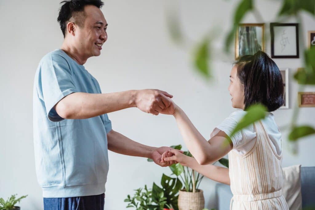 Father dances with his daughter in their living room. They are having a dance party which is a great game for autistic kids.