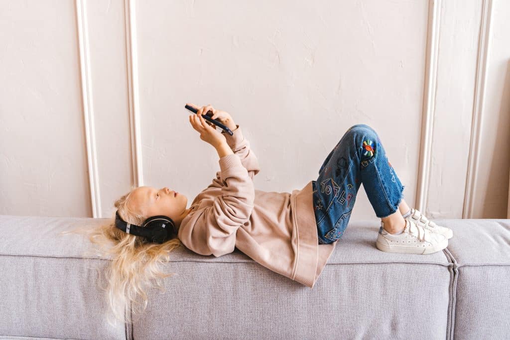 Gifts for kids with ADHD this image shows a child lying on a cushion while using a phone and wearing headphones