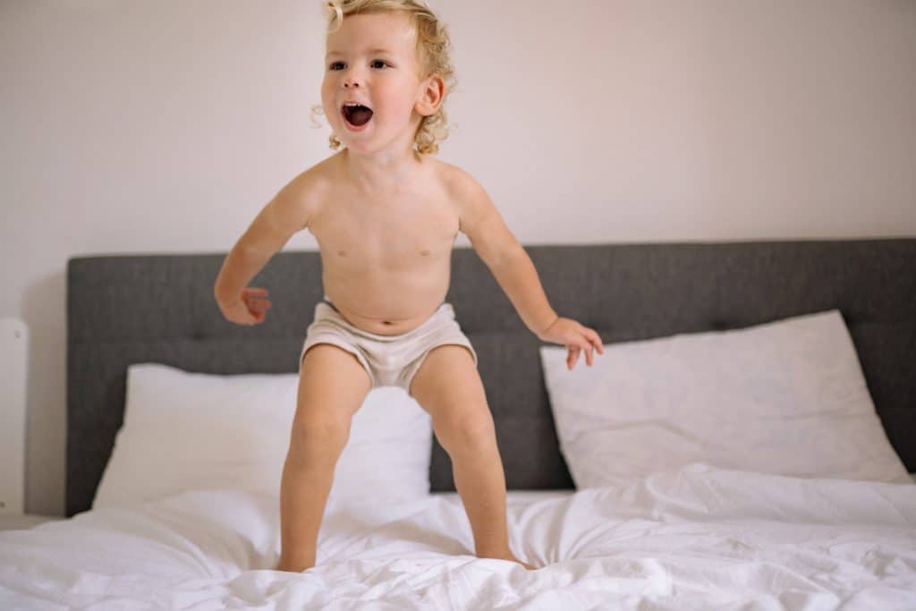 Potty training this image shows a little boy  standing on the bed
