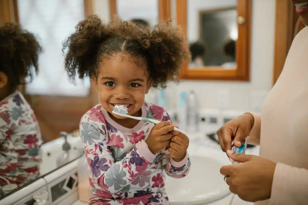 How do you explain personal hygiene to a child? A mom shows her little girl how to brush her teeth.