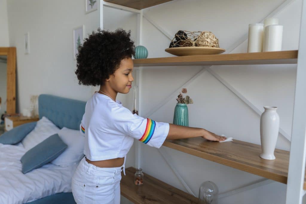 How to improve a child's memory? A young girl cleans a shelf as part of a cleaning routine to improve memory.