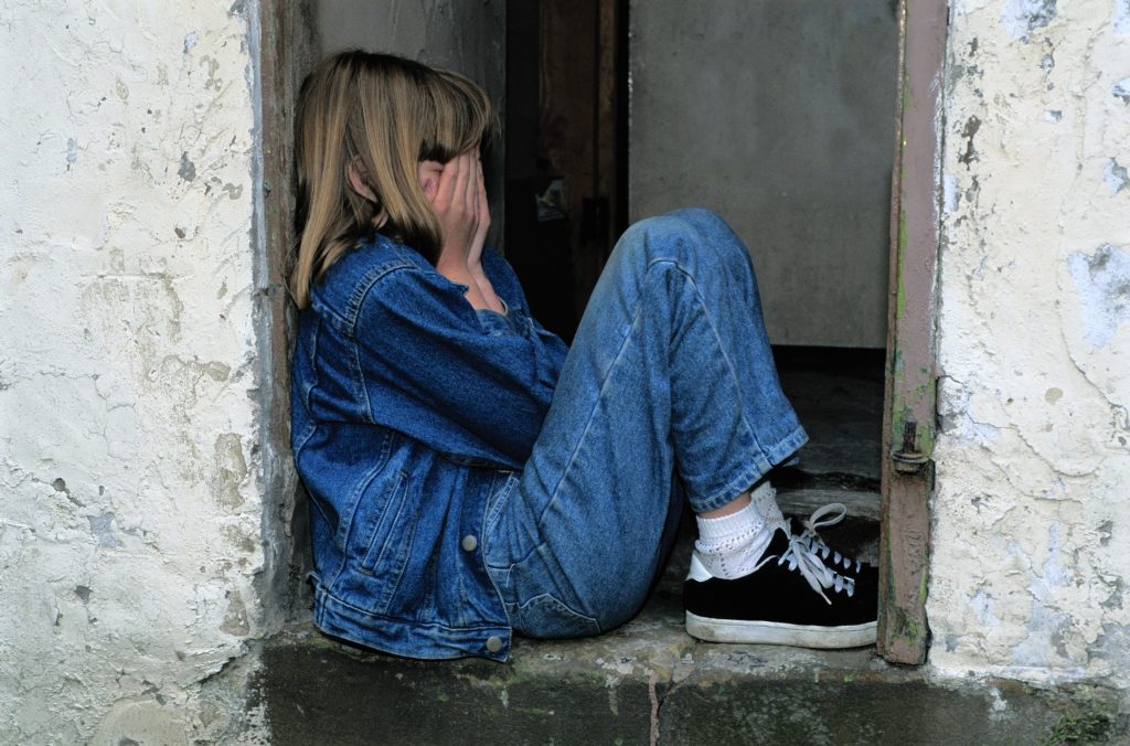 How to deal with rejection sensitive dysphoria: A young girl sits on the floor of a door way, and covers her face with her hands.