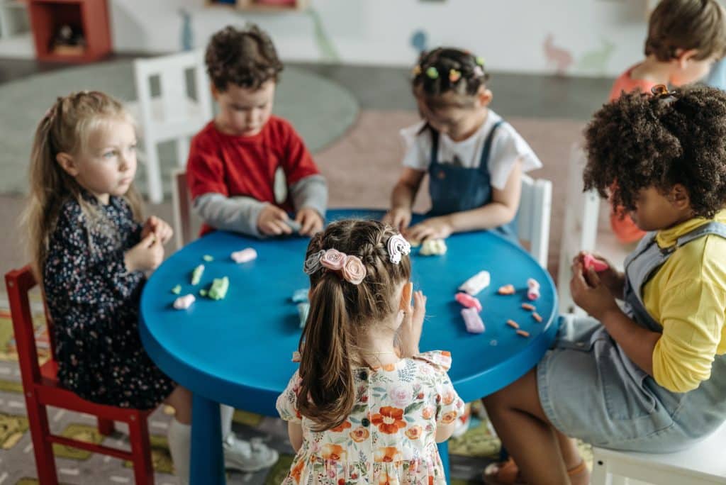Six kids sit around a table learning with tactile dough in a schools for kids with autism.