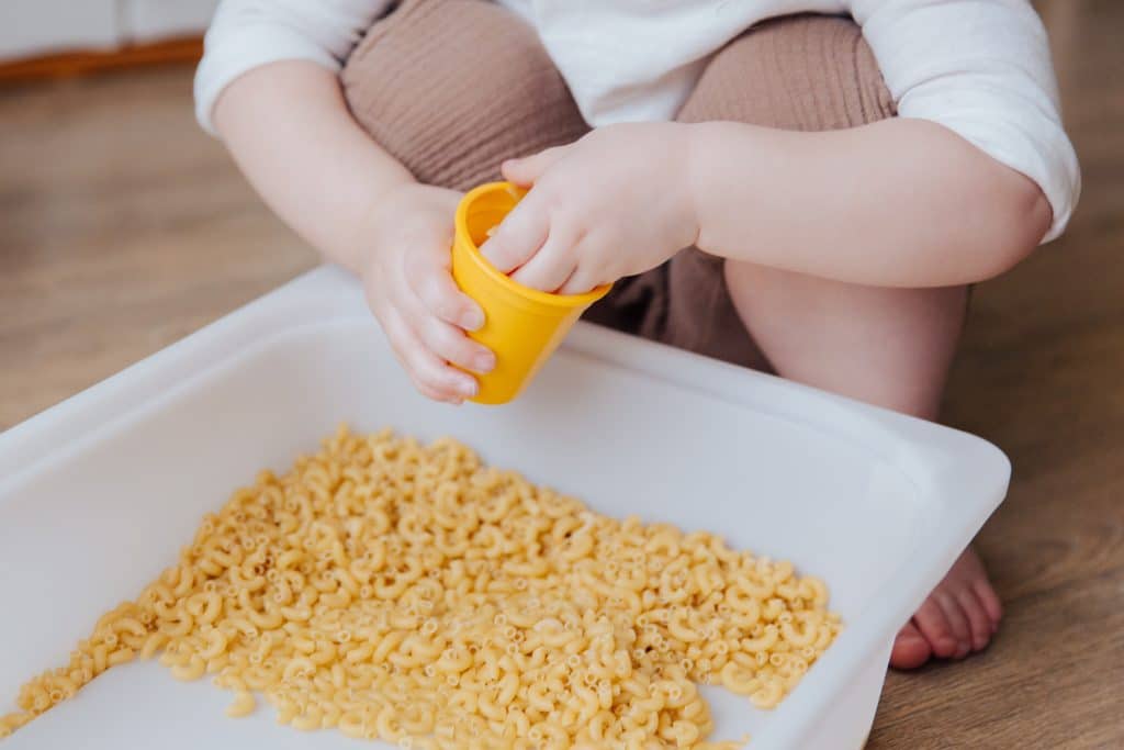 Sensory sensitivities can cause children to be drawn to or repulsed by certain textures like macaroni that this child is playing with.