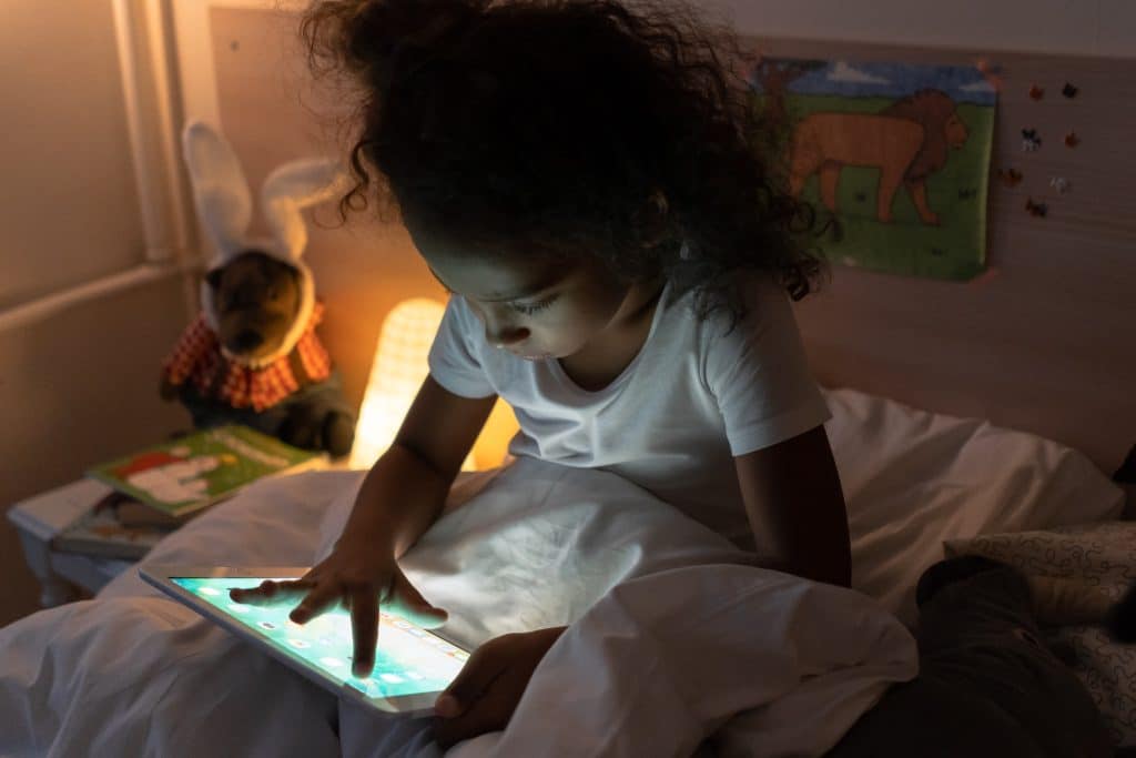 Sleep medication for autistic child. A little girl sits up in bed at night and plays on a tablet.