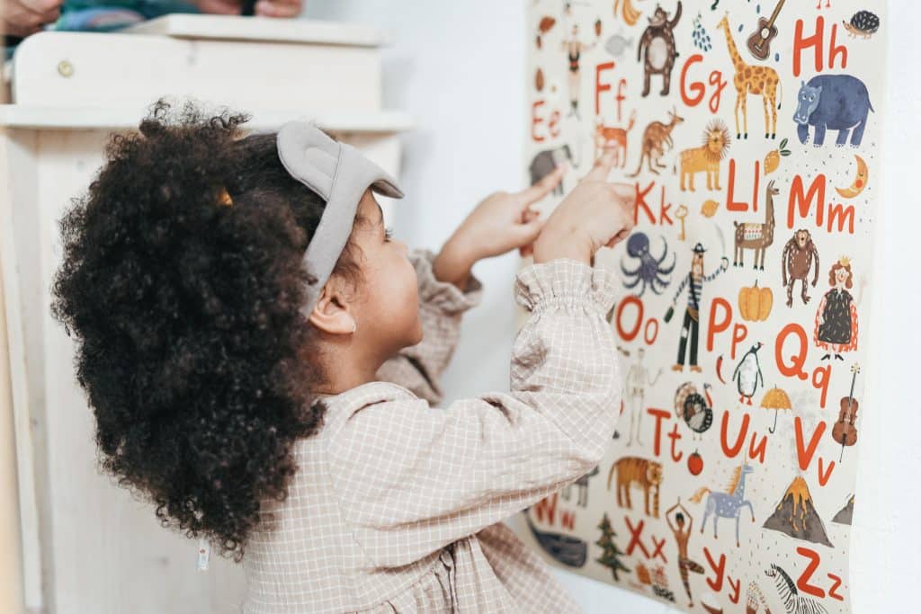 How to teach sight words kindergarten: A little girl points to and looks at a poster with the alphabet and pictures.