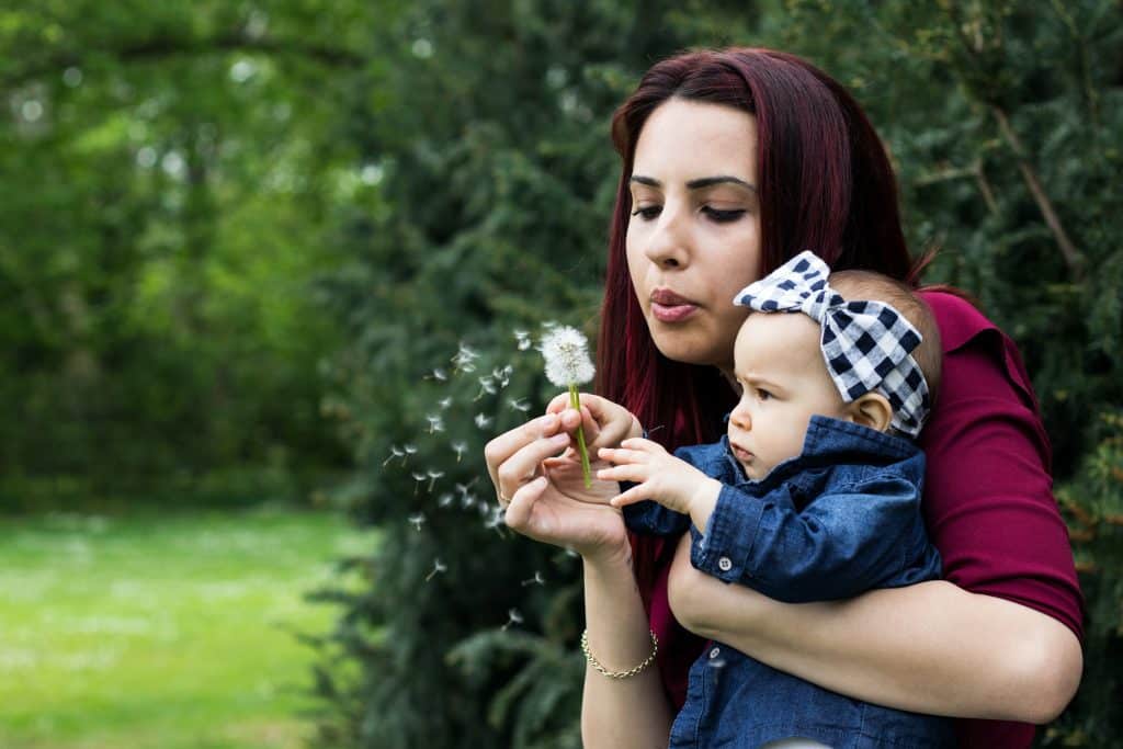 Is ADHD overdiagnosed in children? A young mom holds her baby and blows a dandelion flower.