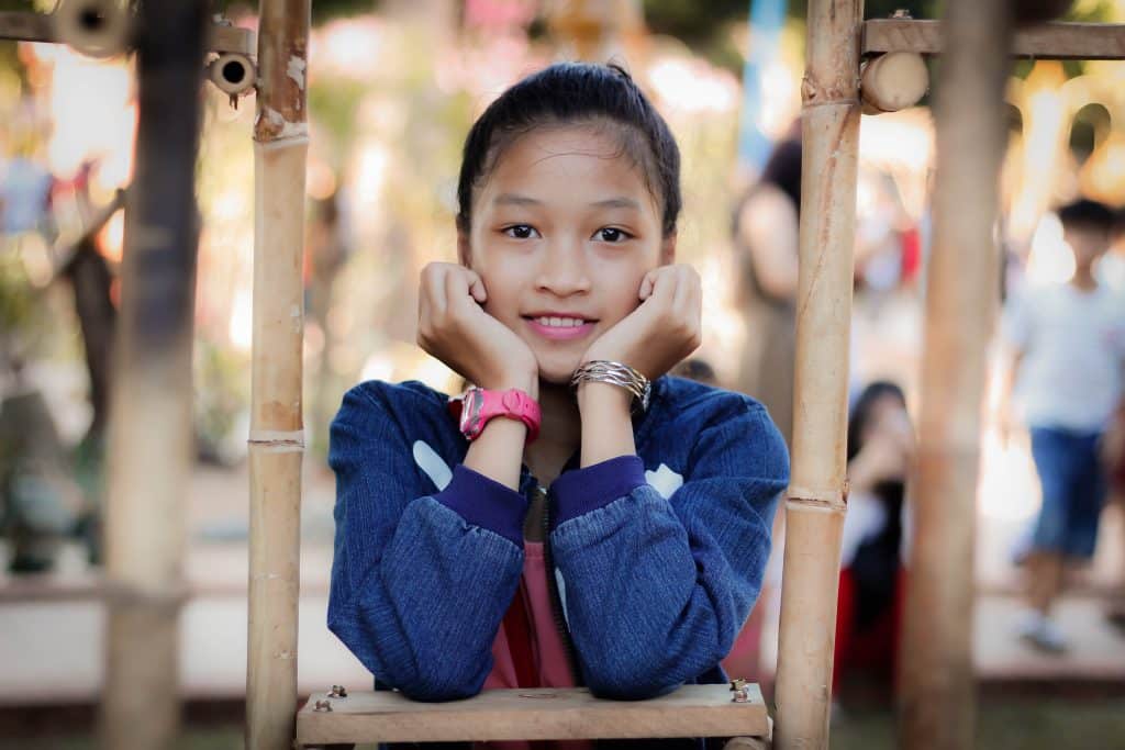 ADHD and rejection sensitivity: an adolescent girl rests her head on her hands and smiles at the camera.