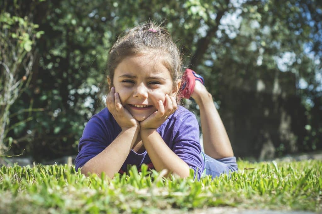 Is a child with ADHD considered special needs? A little girl lays on her stomach in the grass, smiling at the camera.