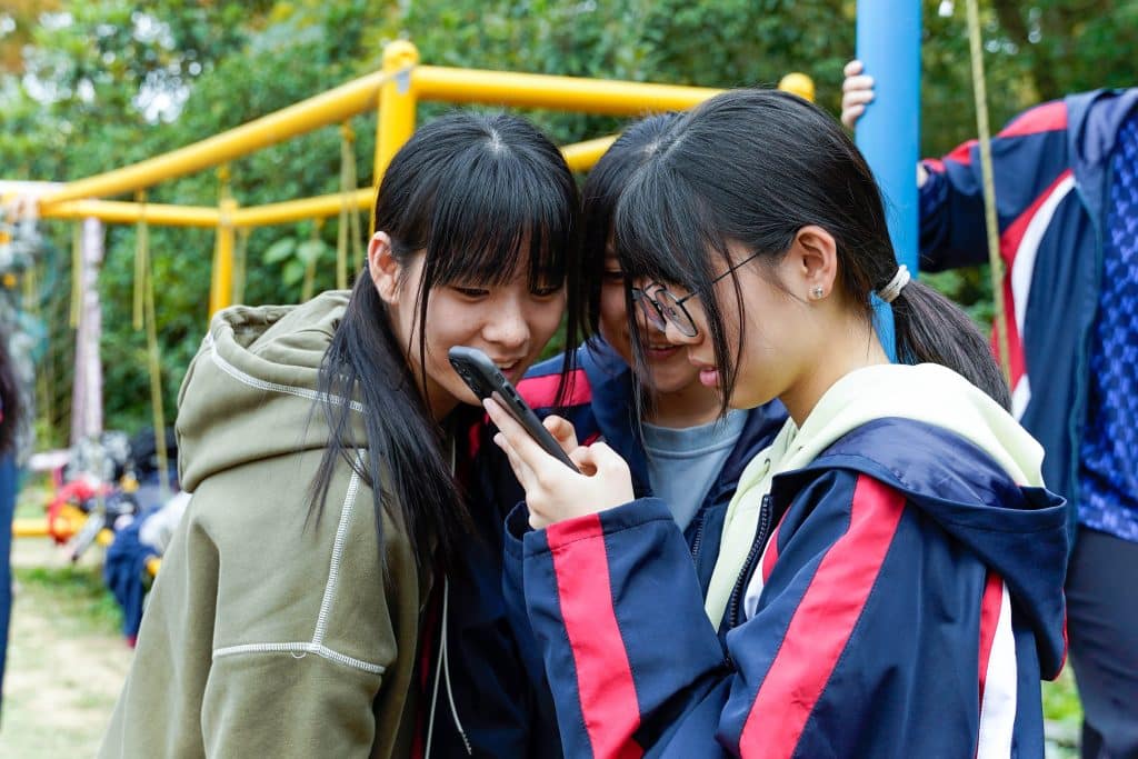 Autism in teenage girls: A group of three teenage girls gather around one girl holding a cell phone.