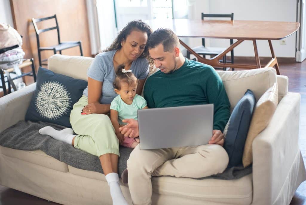 Babies with down syndrome: A mom and dad sit on their couch with their baby girl, and look up information on a laptop.