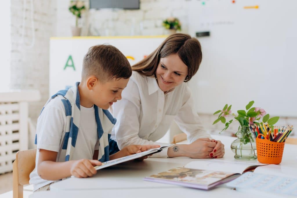 A teacher smiles at her student who is reading some books about adhd for kids .