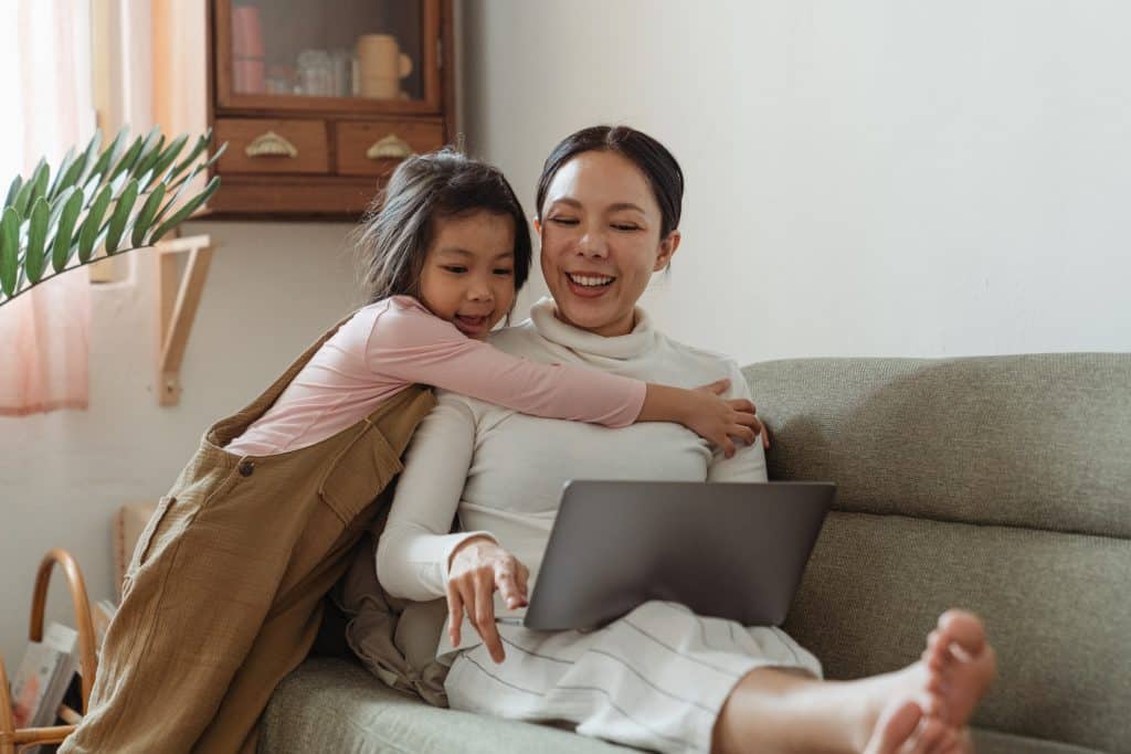 struggles of being a special needs parent. A mom sits at the computer on the couch with her daughter.