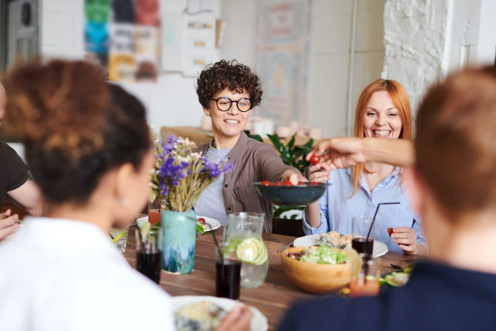 A woman sits at table with other adults, and passes a bowl of fruit; this gathering is a way she copes with the struggles of being a special needs parent.