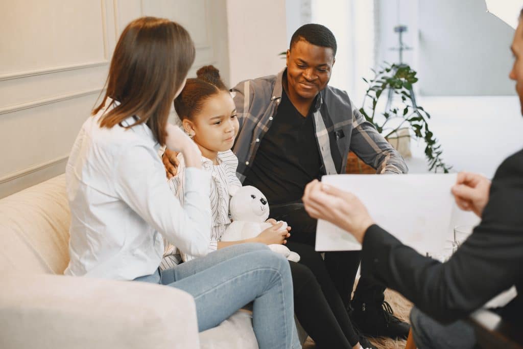 Can you treat ADHD without medication? A dad, mom, and daughter sit on a couch together looking at a piece of paper, therapy.