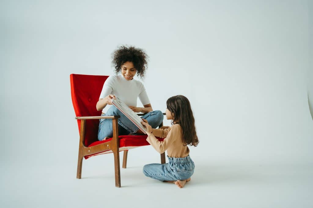 book apps for kids. a mom and daughter read a book while the mom sits in a red chair.