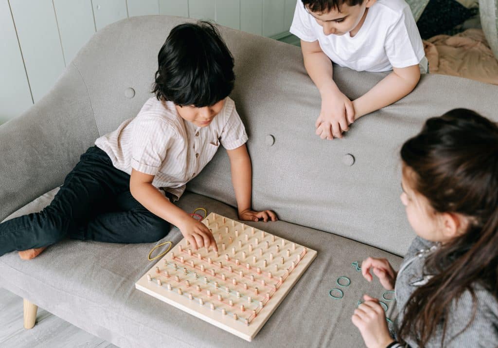 three kids play with a rubber band game together on the couch.