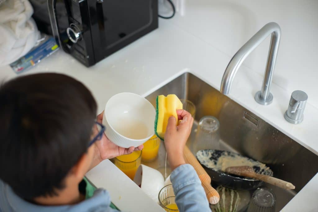 load the dishwasher. A boy is rinsing the dishes before he puts them in the dishwasher.