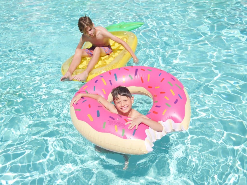 two kids go to the pool together. They each are floating around in a floating device in the pool.