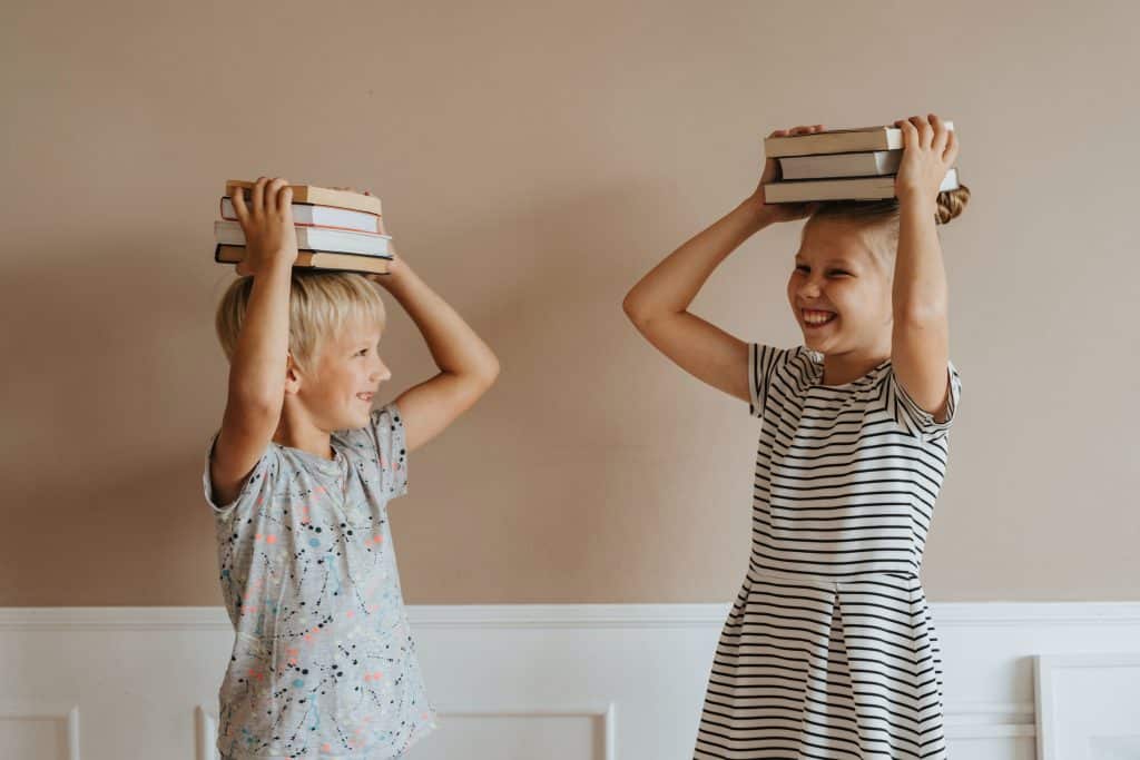 life skills for kindergartners. two kids are putting books on their heads while laughing.
