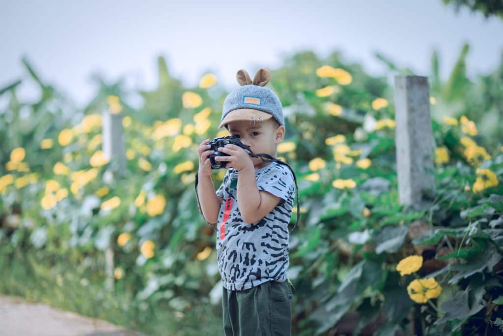 How to dress for warm weather. A child with a camera stands in a field of flowers.