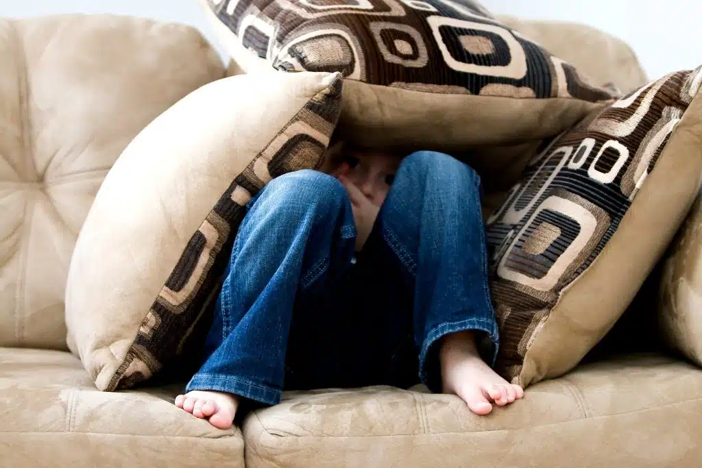 Signs of anxiety in kids. A child hides under a mountain of pillows.