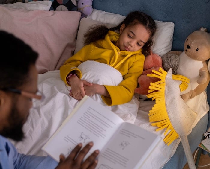 bedtime routine for kids. a story being read to a young girl by her father at bedtime.
