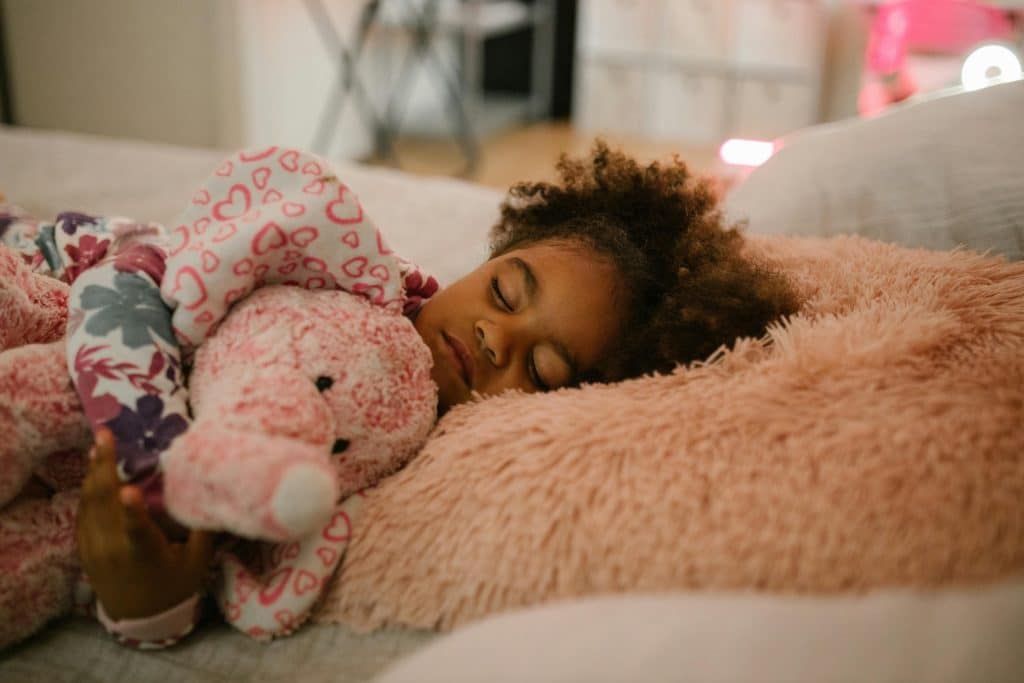 sleep hygiene for kids. a girl is sleeping with her stuffed animal in her bed.