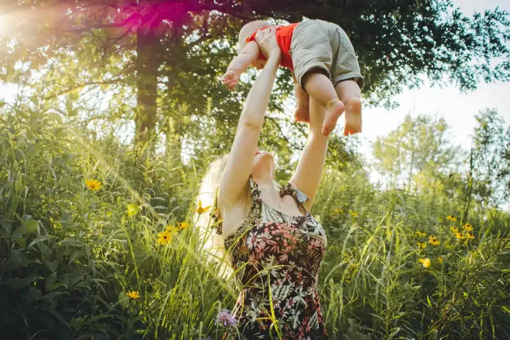 Facts about autism: A joyful woman lifting a child high in the air in a field of wildflowers, symbolizing freedom and happiness