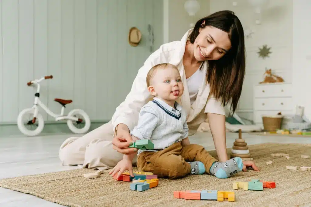 Facts about autism: A smiling woman engaged in play with a young child amongst colorful building blocks, representing learning and development.